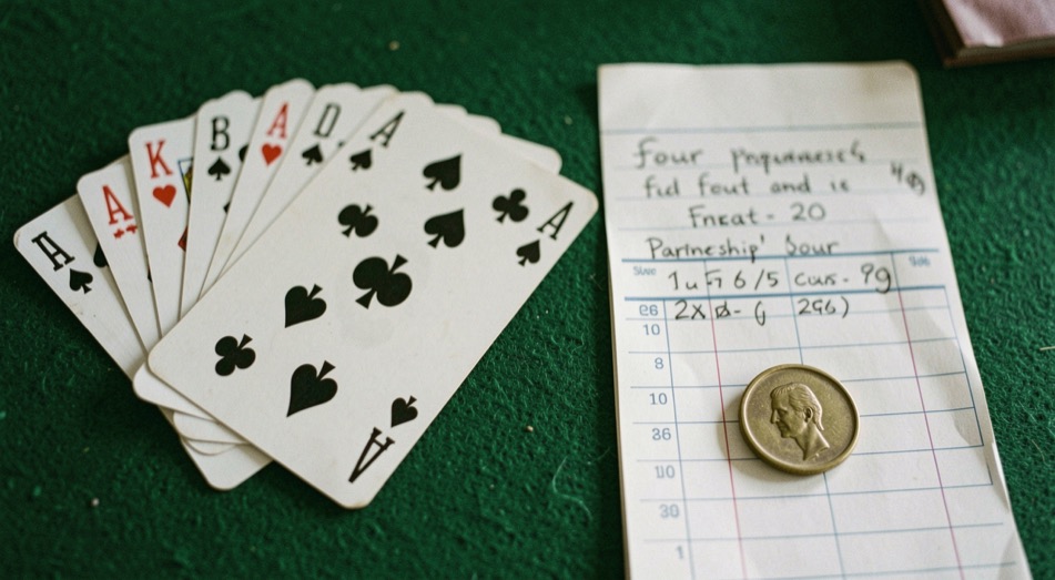 Thirteen card spades hand beside a written partnership bid of four on a score sheet with a small brass token on green felt